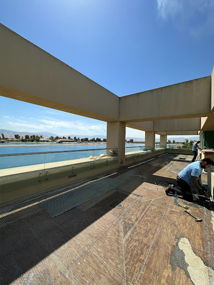 Three construction workers applying bright light blue waterproof coating on outdoor balcony